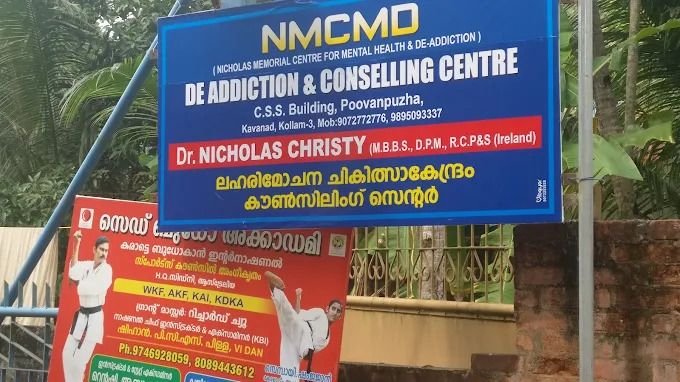 Blue signboard reading NMCMD, Nicholas Memorial Centre for Mental Health and De-Addiction, De Addiction and Counselling Centre, with the address, phone numbers and Dr. Nicholas Christy's name